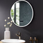 Image shows angled view of round mirror over bathroom vanity.  Edge of mirror is illuminated by LED.