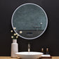 A round mirror is affixed above a bathroom vanity. The LED lighting around the edge of the mirror is on dim.