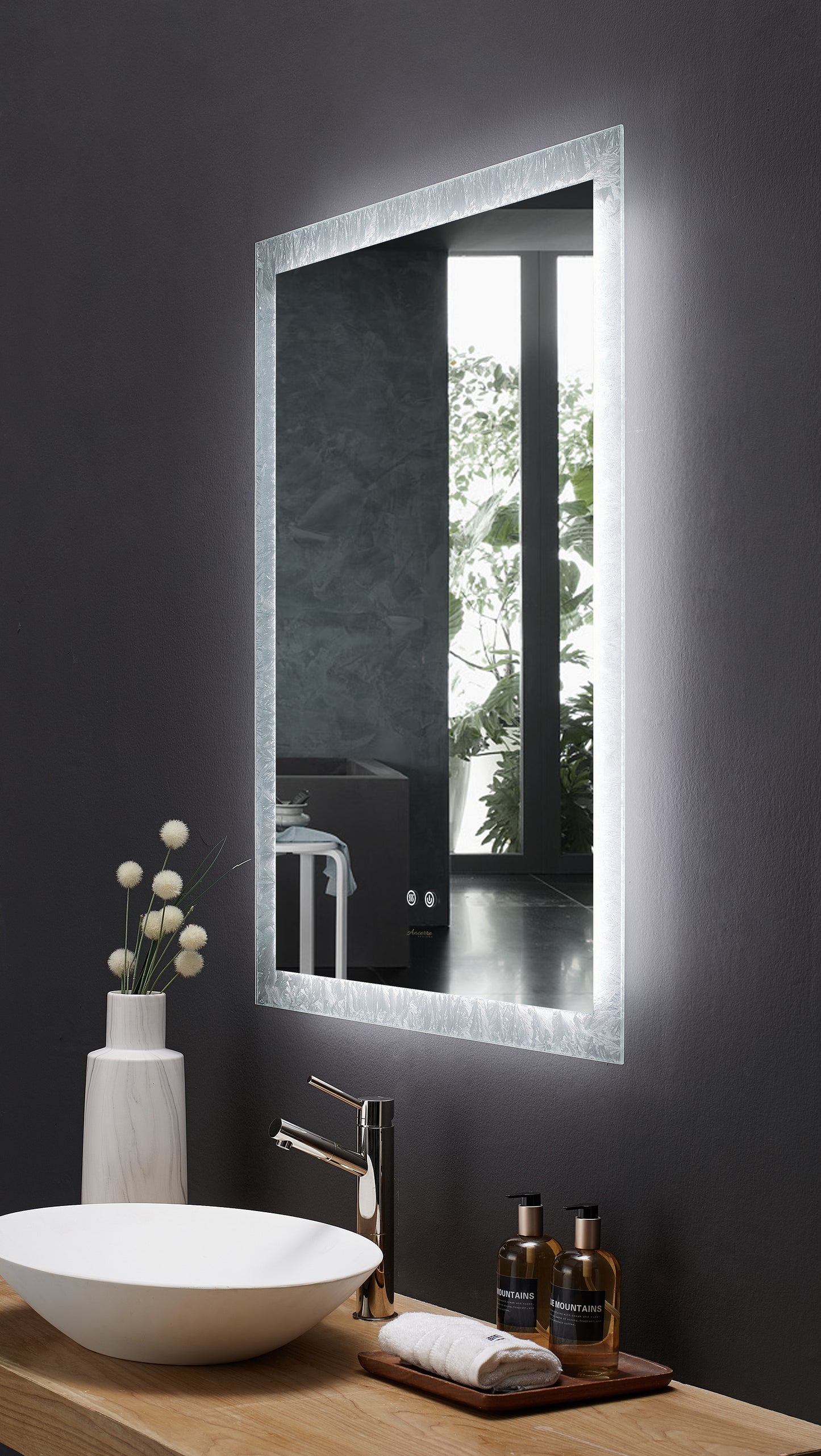 Image is a sharp angle view of a rectangular Ancerre Frysta mirror above a bathroom vanity.  LED edge lighting is on.