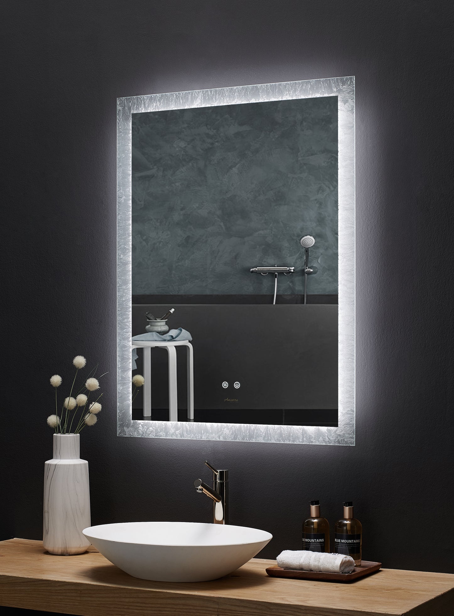 Image is a side angle view of a rectangular Ancerre Frysta mirror above a bathroom vanity. LED edge lighting is on. 