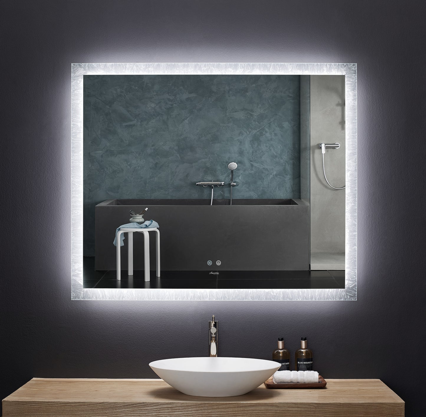 Image shows rectangular mirror—wider than tall—with LED illumination on perimeter.  Mirror is mounted above bathroom vanity.